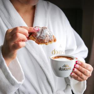a woman holding a pastry and a cup of coffee at Doanesia Premium Hotel & Spa in Tirana