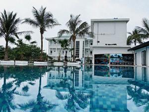 a swimming pool in front of a building with palm trees at Rose Resort in Quat Lâm Ha