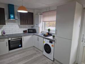 a kitchen with white cabinets and a washer and dryer at My Glasgow House Robroyston in Hogganfield
