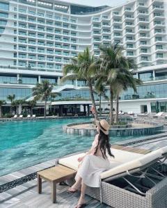 a woman sitting on a bench next to a swimming pool at Anna Belle Đồi Rồng Hotel - Homestay chuỗi HPT Home Hải Phòng in Kon Rung (1)