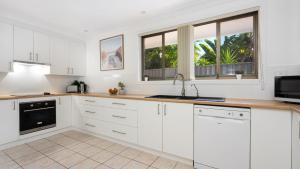 a white kitchen with white cabinets and windows at Coastal Crush in Callala Beach