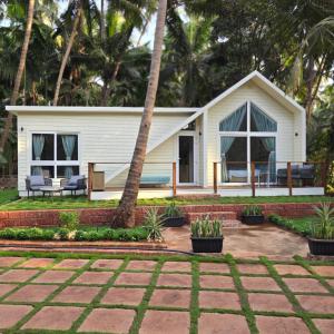 a small white house with a patio and palm trees at Sea Breeze, Guhagar in Guhagar