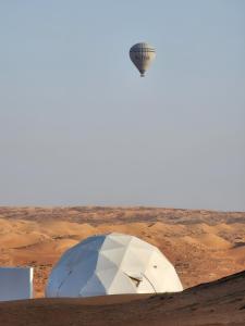 a hot air balloon flying over a tent in the desert at Bubbles Domes Private Cmp in Badīyah