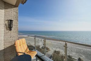 a woman sitting in a chair on a balcony looking at the ocean at Am Südstrand 9 Strandburg I in Burgtiefe auf Fehmarn 