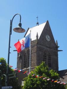 a church with a clock tower and a flag at Chez Léonie in Sainte-Mère-Église