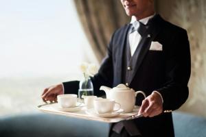 シンガポールにあるThe St. Regis Singaporeのカップの載ったトレイを持つタキシードを着た男性