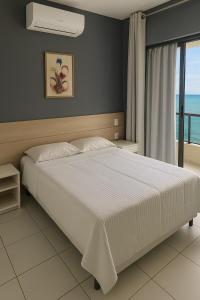 a bedroom with a large white bed and a window at Flat Vista Mar com Piscina e Wi-Fi Rápido Rio Vermelho in Salvador