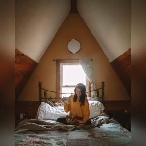 a woman sitting on a bed in a attic at A-Frame #15 - by The Chalets in Logan +16 photos