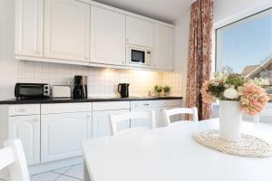 a kitchen with white cabinets and a table with a vase of flowers at Seepferdchen Wulkje in Hansaland +29 photos