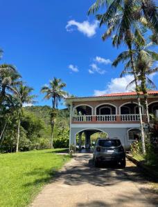 Un coche aparcado delante de una casa con palmeras. en Recanto Dom José, en Peruíbe