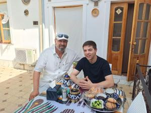 two men sitting at a table with food at Orzu Guest House in Bukhara