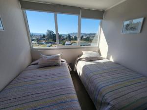 two beds in a small room with a window at Departamento Centro Puerto Montt in Puerto Montt