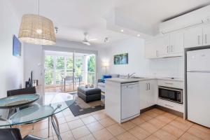 eine Küche und ein Esszimmer mit weißen Schränken und einem Tisch in der Unterkunft Port Douglas Apartments - Adults Only Oasis in Port Douglas