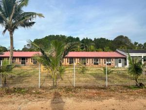 a fence in front of a building with palm trees at OYO 90818 Cemara Puri Resort & Spa in Kampong Pantai Batu Hitam
