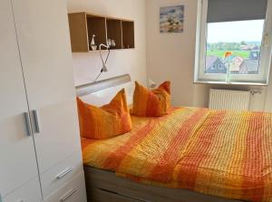 Un dormitorio con una cama con almohadas naranjas y una ventana. en Tief 10 Meeresbrise 402, en Wangerland 65 fotos más