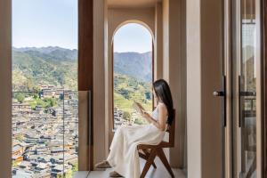 a woman sitting in a chair reading a book in a window at Seven Letters Preface Hotel Xijiang Qianhu Miao Village in Xijiang