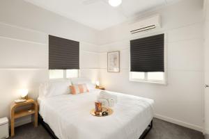 a white bedroom with a white bed and two windows at Smart Suites Self Check-In Cottage - Carina in Brisbane