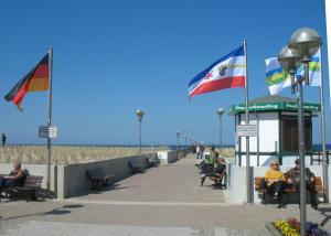 people sitting on benches next to the beach with flags at Küstenwind in Graal-Müritz