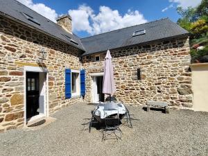 an umbrella and chairs in front of a stone building at Les Hortensias in La Poultière