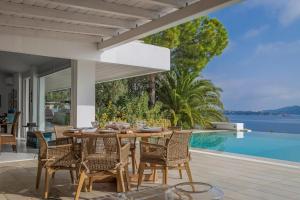 a dining table and chairs on a patio with a view of the water at Super Luxury Skiathos Villa Seven Stunning Bedroom Suites Villa Daphne Achliades in Achladies