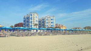 a beach with chairs and blue umbrellas and buildings at Cortina 2-9 in Lido di Pomposa