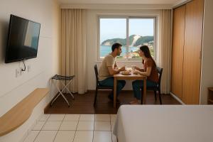 a man and woman sitting at a table in a hotel room at Ponta Negra Flats Partic in Natal
