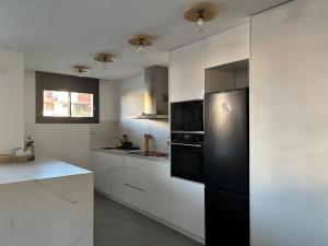 a kitchen with white cabinets and a black refrigerator at Casa con piscina y parking en Roda de Berà in Roda de Bará
