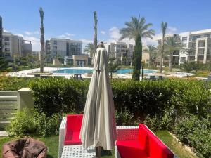 un parapluie blanc à côté de deux chaises rouges dans l'établissement 1 Bedroom Ground in Marassi Marina 1, à El Alamein