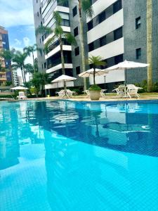 a large blue swimming pool with chairs and umbrellas at Riviera 200m Praia Serv de Praia and Pisc Aquec in Bertioga