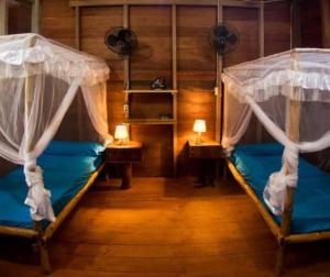 two beds in a room with two tables and two lamps at Playgrounds Sabbit Mentawai Surfcamp in Pulau Masokut