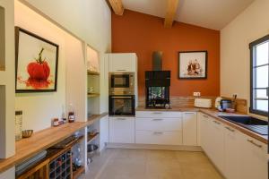 a kitchen with white cabinets and an orange wall at Le Montebello de Paradou in Paradou
