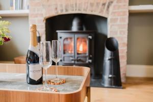 a bottle of wine and two wine glasses on a counter with a fireplace at Herdsman's Cottage - Beautiful 3 Bed in Wiltshire! in Sherston