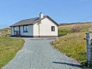 a small white house in a field with a gravel road at Ardmore Holiday Cottage in Trumpan