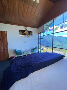 a bedroom with a bed with two chairs and a large window at Nivriti Stays in Kanatal