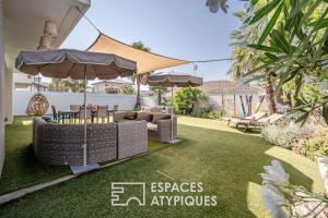 a backyard with a lawn with wicker furniture and an umbrella at Villa proche plage mer, piscine grand terrain Capao Hotel in Cap d'Agde