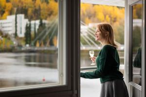 a woman holding a glass of wine looking out of a window at Finlandia Hotel Alba in Jyväskylä