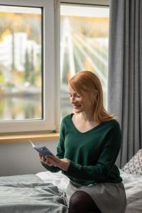 a woman sitting on a bed holding a tablet at Finlandia Hotel Alba in Jyväskylä