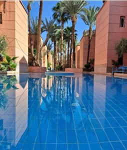 a swimming pool with palm trees and a building at Riad Emeraude Cozy Riad with Shared Pool 4 Room in Marrakech