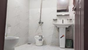 a white bathroom with a toilet and a sink at Aangan Residences in Skardu