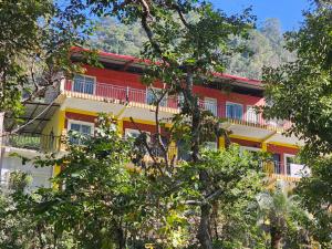 a red and yellow building with trees in front of it at Tapovan Cascades Yogvillage homeStay in Rishīkesh