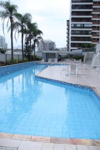 Una gran piscina azul con sillas y palmeras. en Flat Residencial Praia da Barra, Piscina e Sauna - Frente Mar D68508, en Río de Janeiro