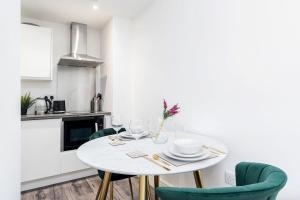 a white kitchen with a white table and green chairs at Central Apartment - Sheffield in Sheffield