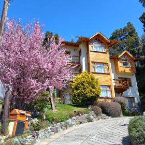 a large house with pink flowering trees in front of it at Apart Hotel Bungalows Los Cipresales in San Carlos de Bariloche