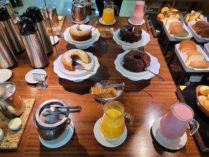 a wooden table topped with plates of cakes and orange juice at Premium Hotel Frutal in Frutal