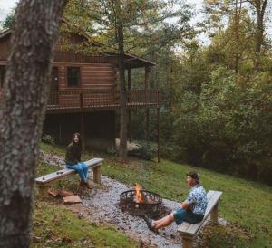 two people sitting around a fire in front of a cabin at Hemlock - by The Chalets in Logan