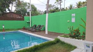 a swimming pool with chairs next to a green wall at Caminho do Paraíso in Porto De Galinhas