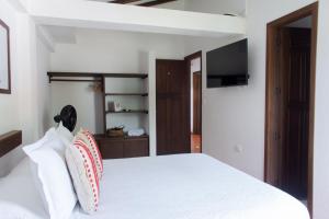 a bedroom with a white bed with pillows and a television at Casa Chevere Hostel Boutique in Barichara