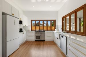 a white kitchen with white appliances and wooden floors at Sunnyside On Burns - Central,Farmers Market, Beach in Byron Bay