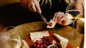 a person cutting cheese on a table with a glass of wine at voco Auckland City Centre by IHG in Auckland +49 photos