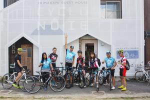 grupa ludzi stojących z rowerami przed budynkiem w obiekcie Cyclo No Ie w mieście Imabari